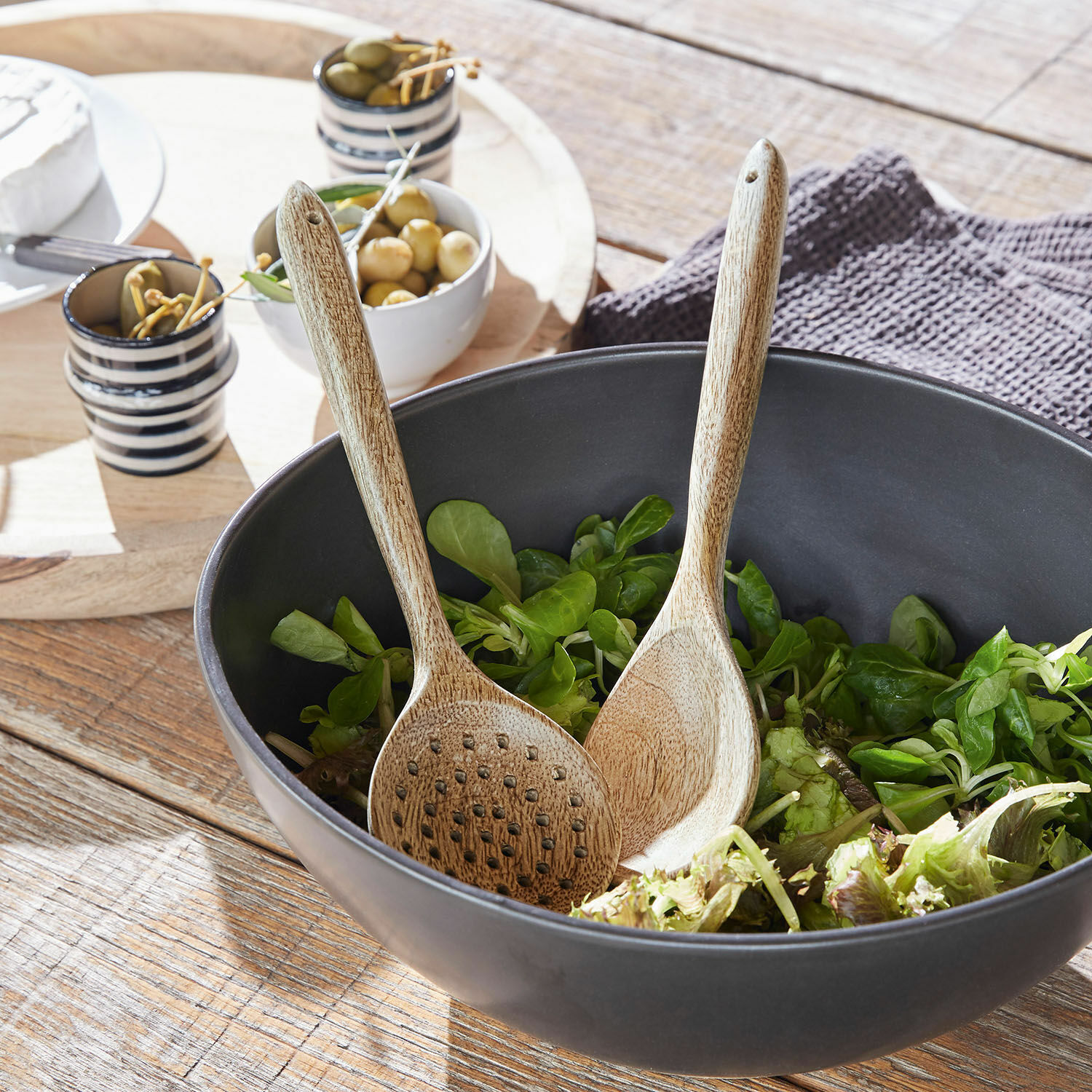 Saladecouvert Helier Zwarte houten kom met groene salade en houten lepels op rustieke houten tafel