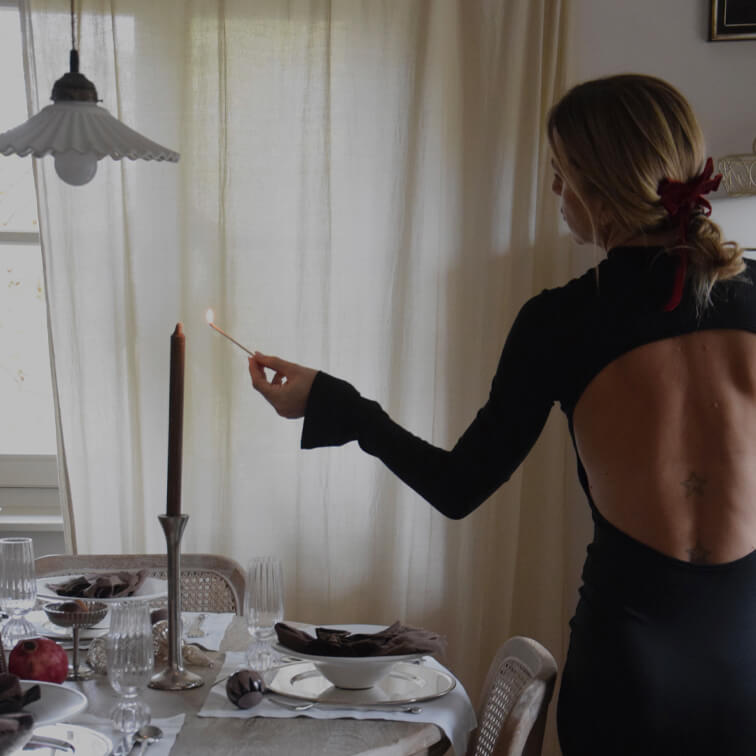Vrouw in zwarte jurk met open rug steekt kaars aan op een elegant gedekte eettafel