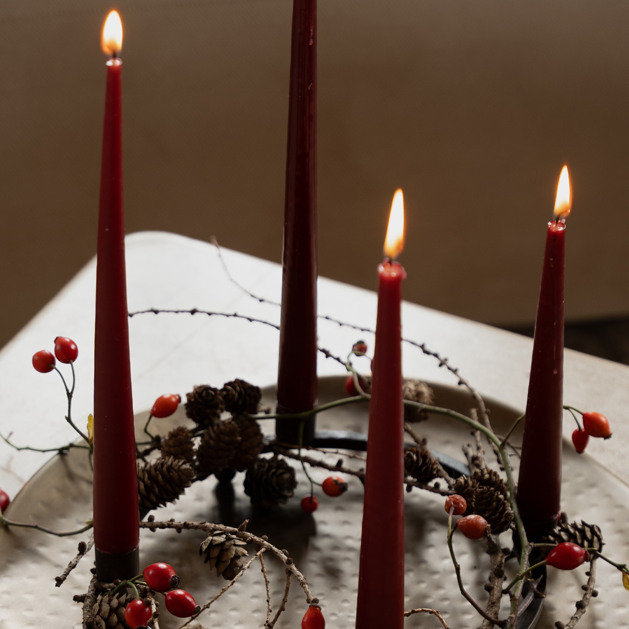 Rode adventskaarsen met dennenappels en rode bessen op metalen standaard op tafel