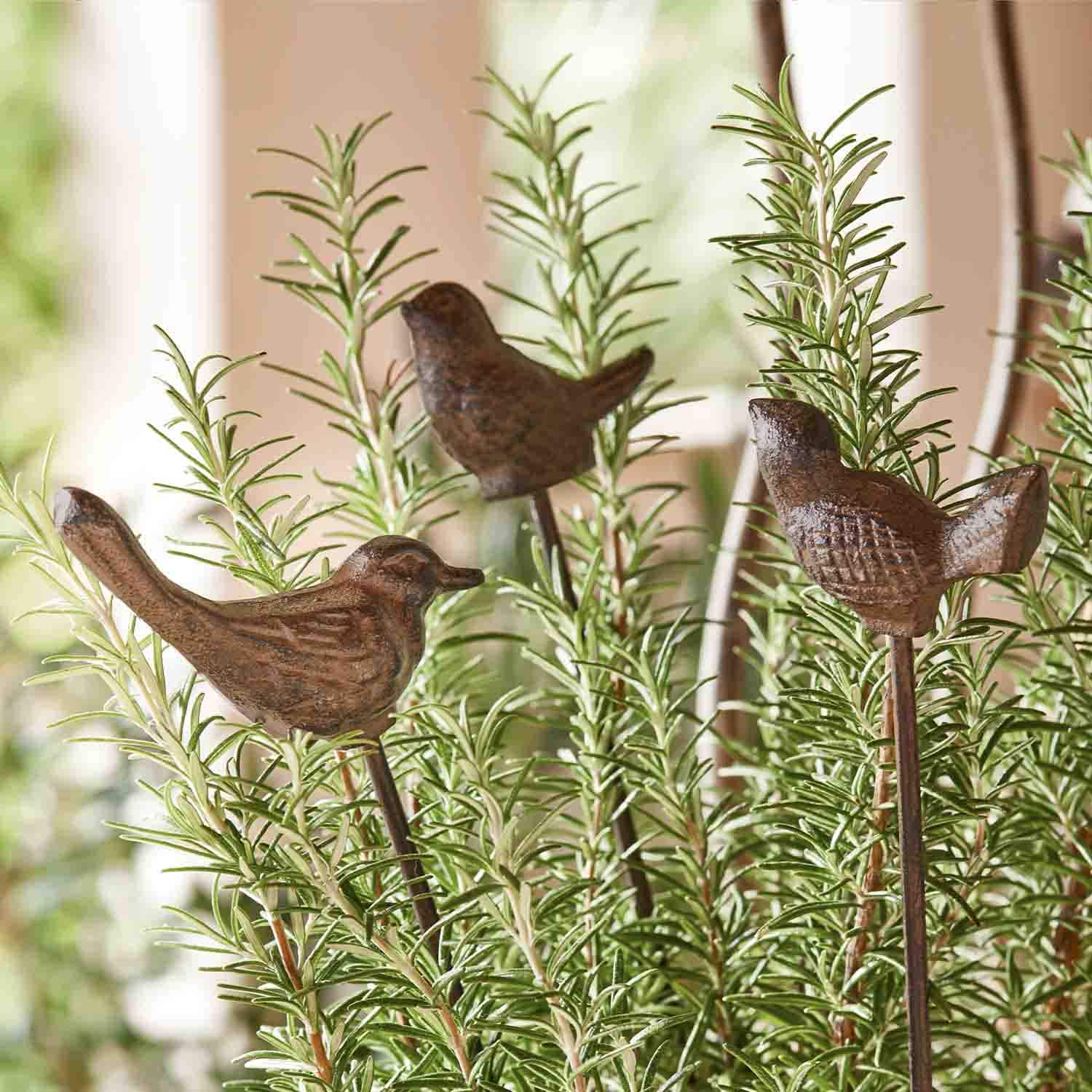 Decoratieve bruine metalen vogeltjes op stokjes tussen groene rozemarijn takken