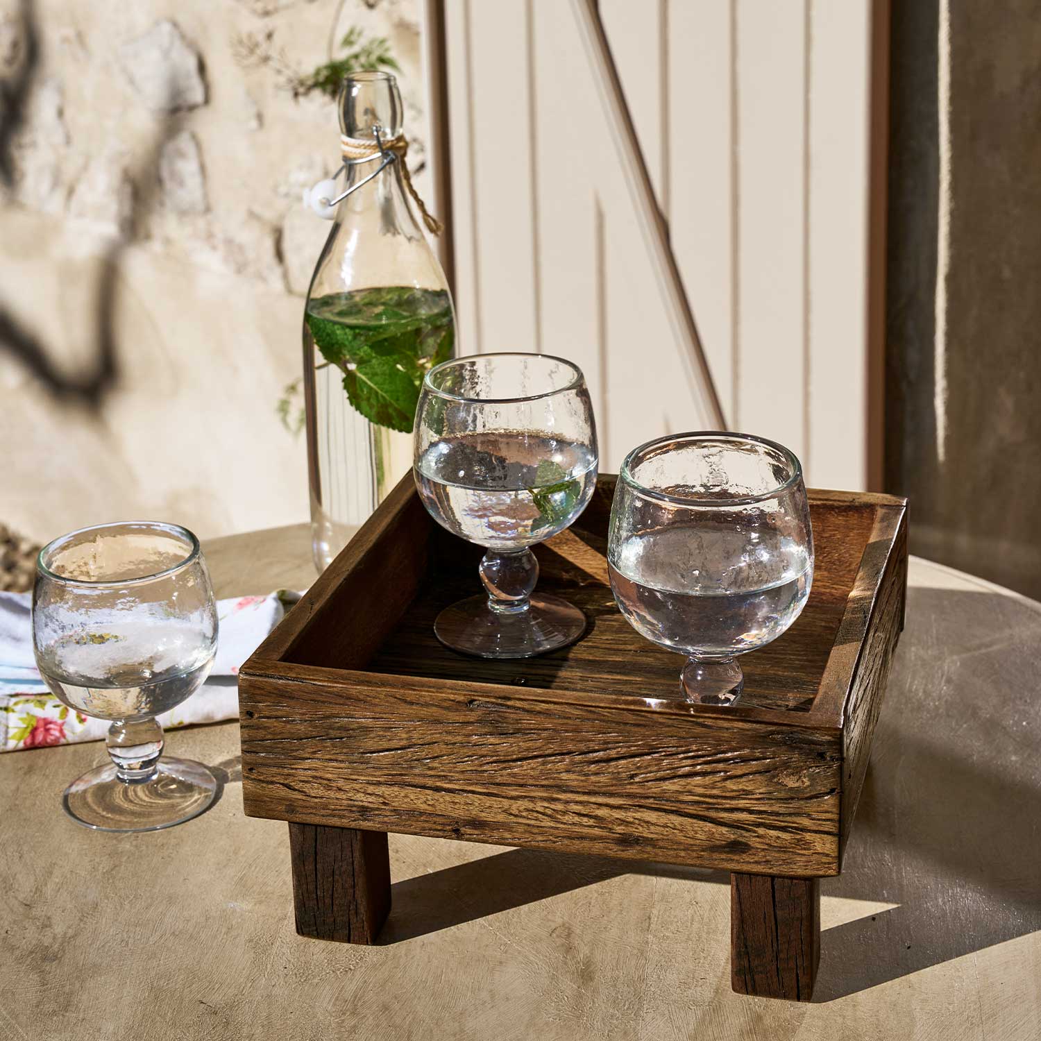 Houten dienblad op poten met drie glazen en een fles water met munt op tafel