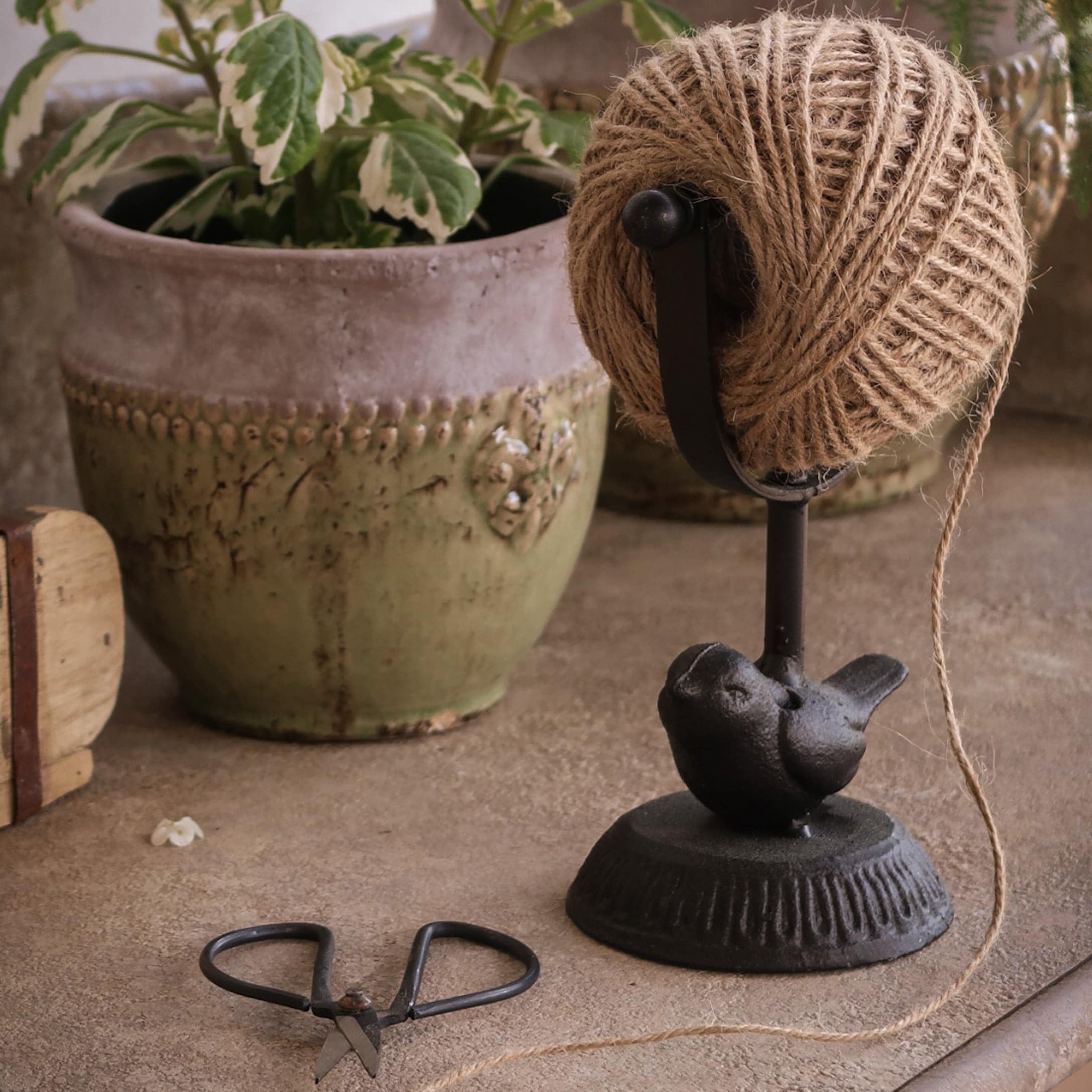 Zwarte metalen houder met touw en vogelornament voor een groene bloempot