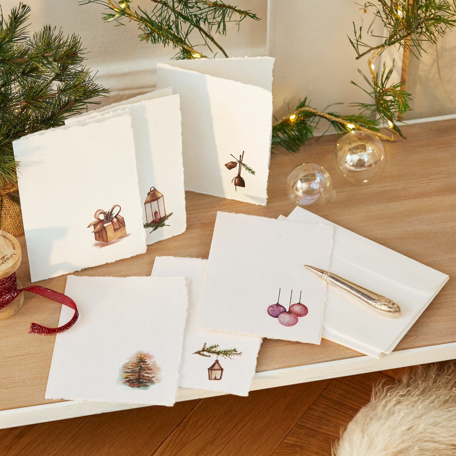 Wenskaart set van 6 Aeloria Set witte kerstkaarten met motieven van boom en cadeaus op houten tafel met LED-lichtjes