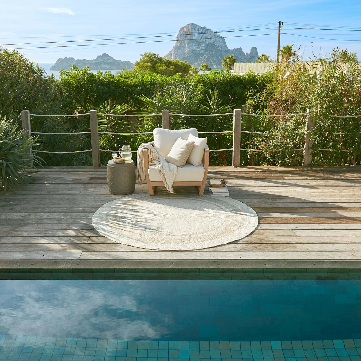 Houten terras met witte stoel en ronde vloerkleed bij zwembad met uitzicht op bergen en groen