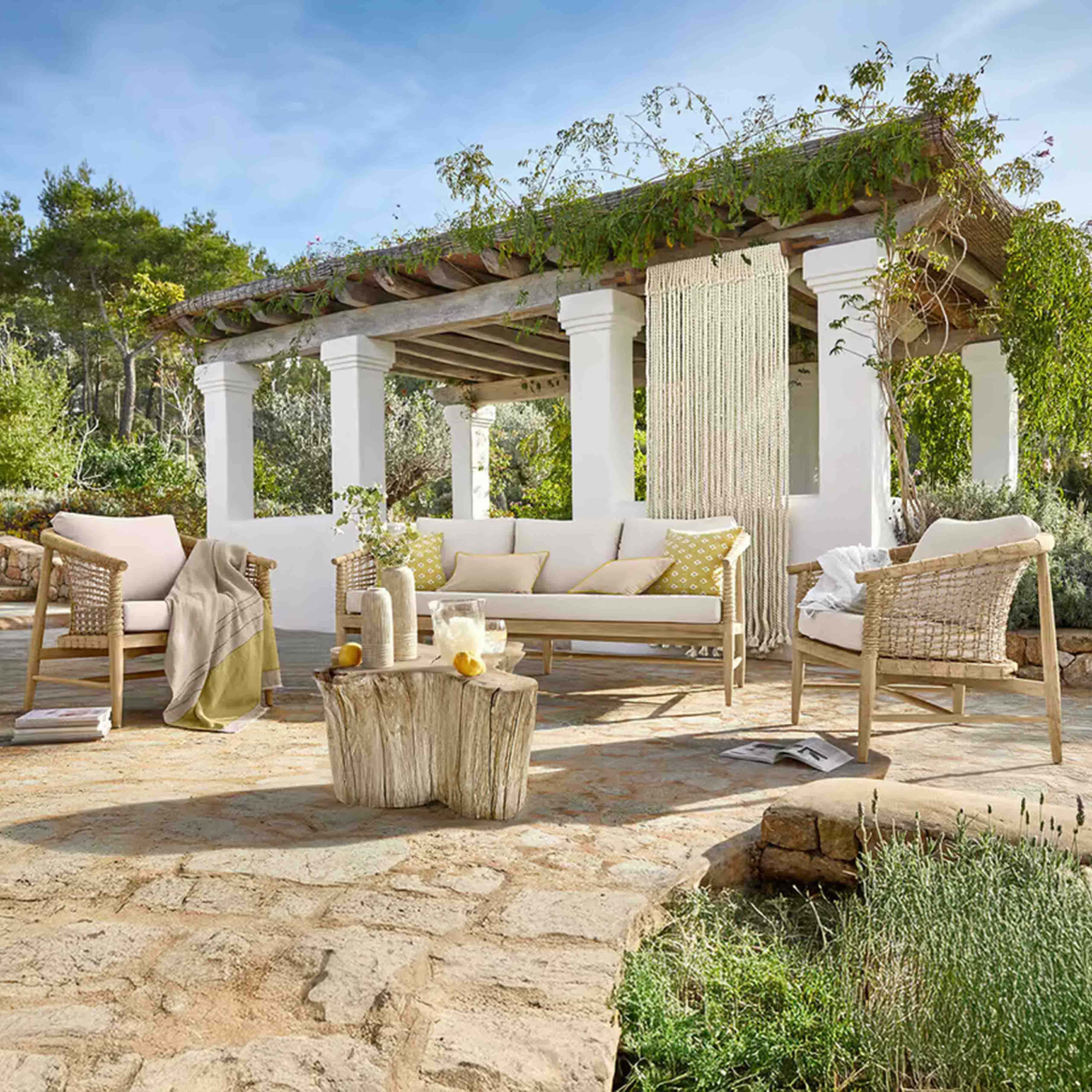 Tuinmeubelset van licht hout met beige kussens op stenen terras onder een pergola met planten