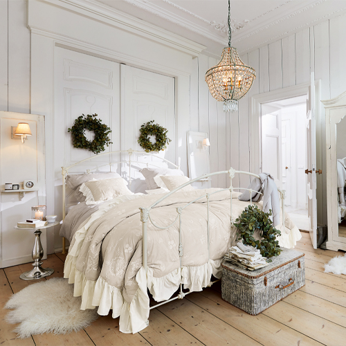 Gezellige slaapkamer met wit metalen bed, beige beddengoed, wanddecoraties en lichte houten vloer