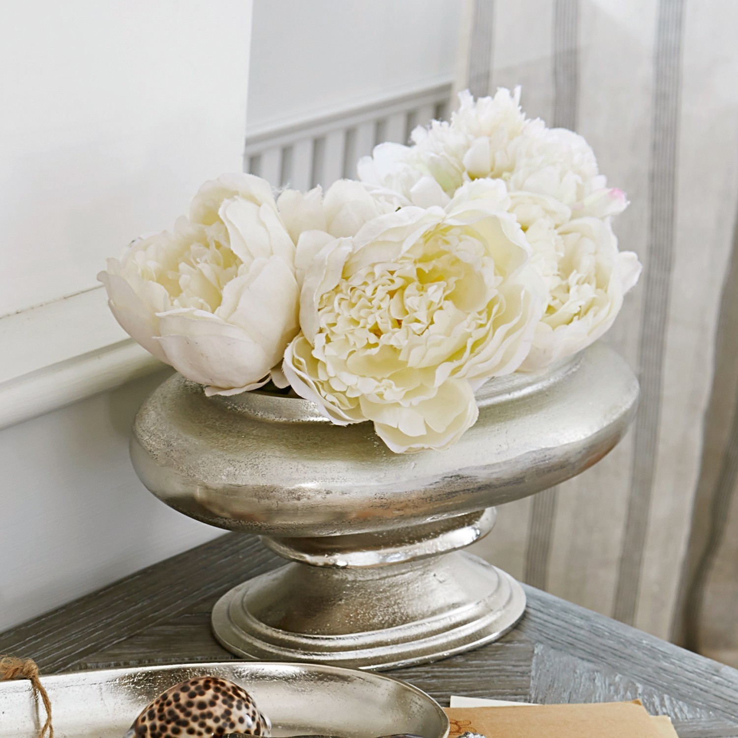 Zilverkleurige metalen decoratieve schaal met witte bloemen op houten tafel in woonkamer