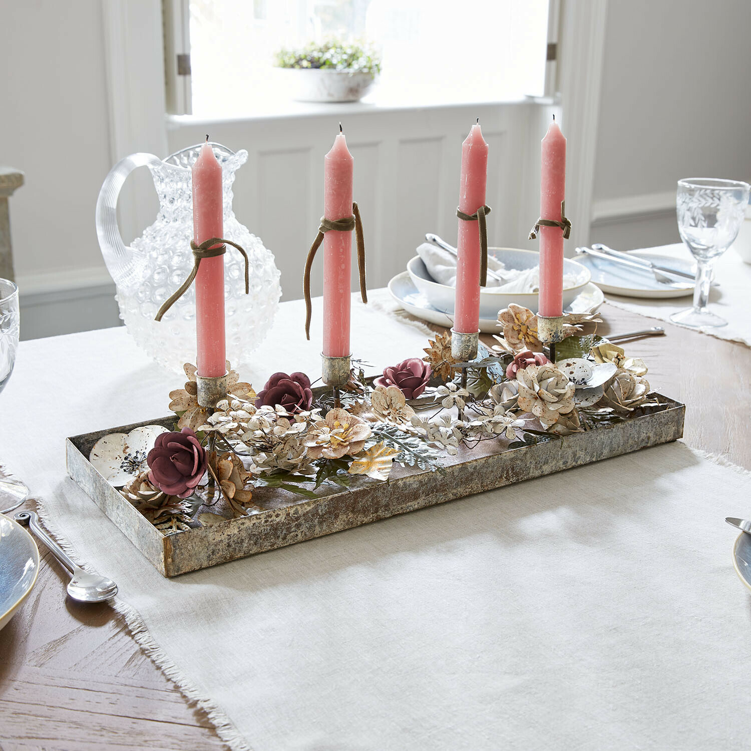 Metalen kandelaar met vier roze kaarsen en bloemendecoratie op eettafel