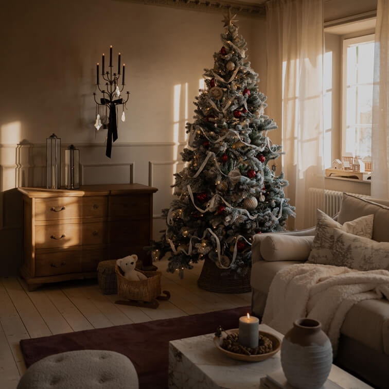 Gezellige woonkamer met versierde kerstboom, houten ladekast en brandende wandkandelaar