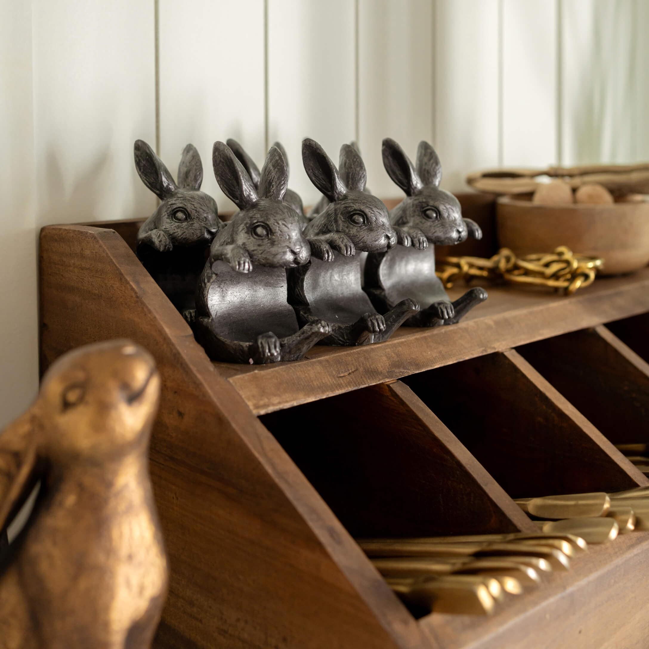 Vier donkergrijze metalen konijnendecoraties op een houten plank met vakken