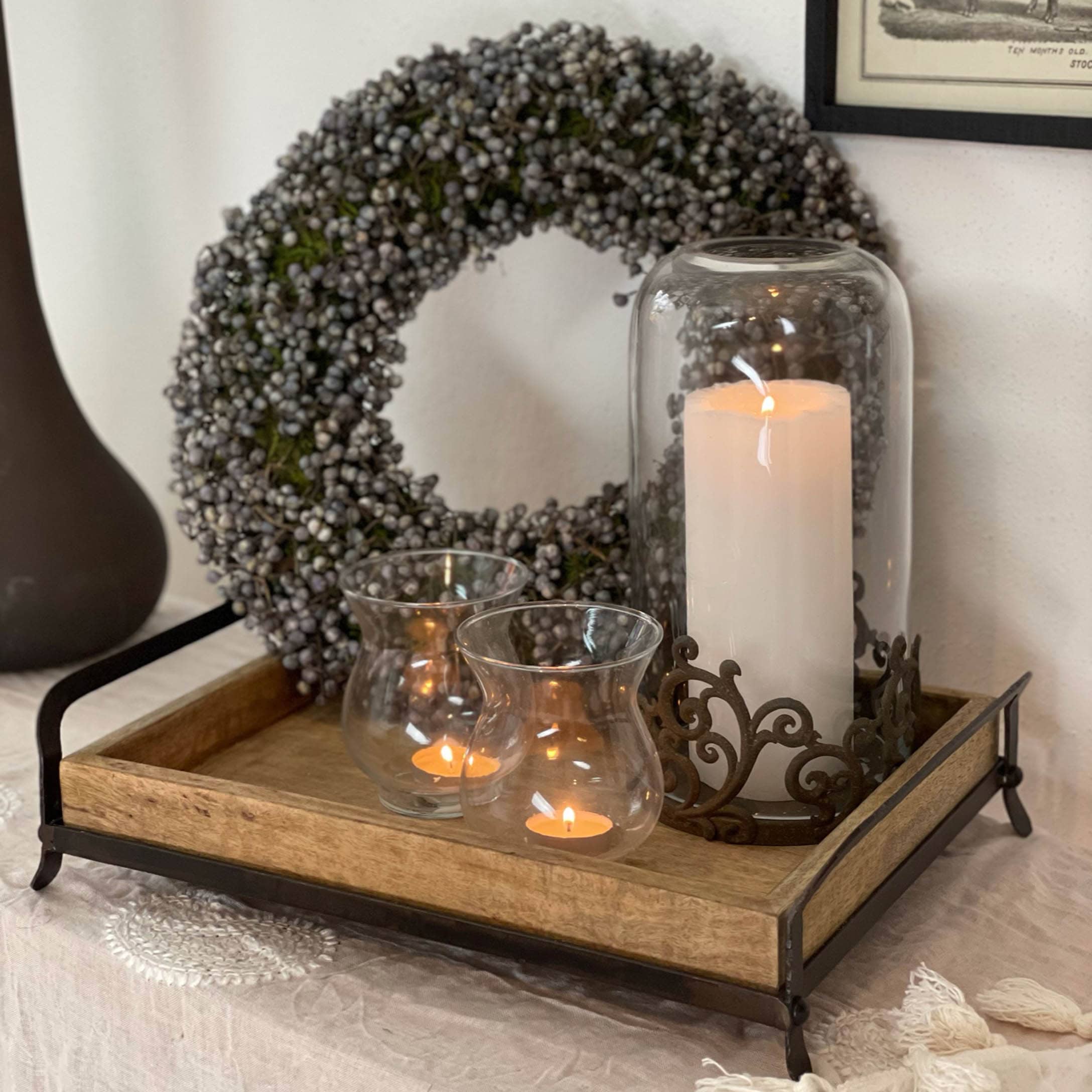 Houten dienblad met metalen frame, decoratieve kaarsen en herfstkrans met grijze bessen