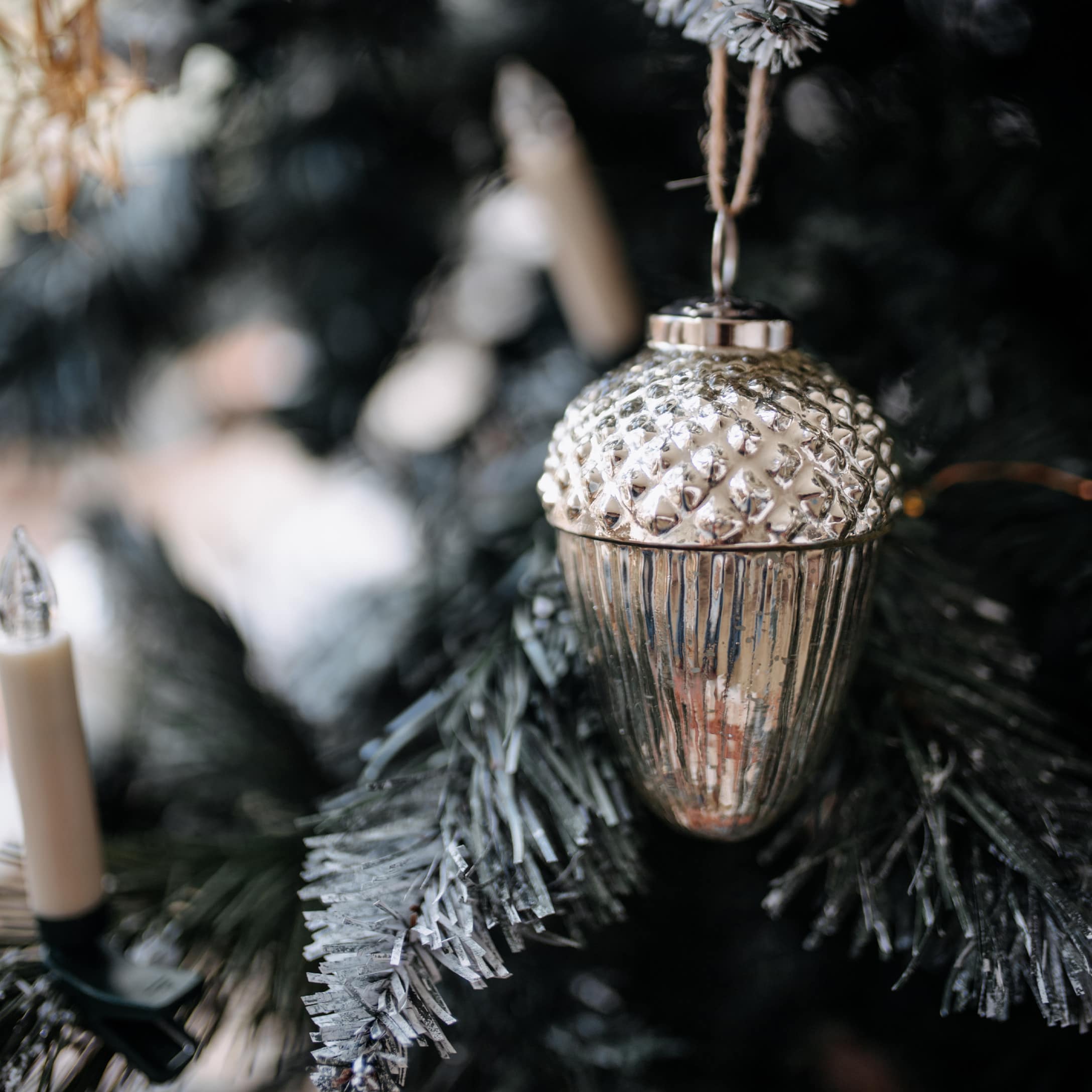 Zilveren kerstbal in eikelvorm met textuur, hangend aan groene dennentak
