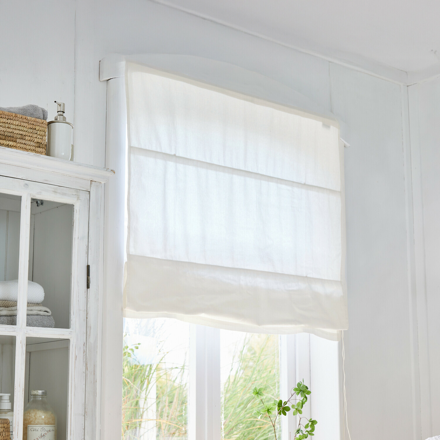 Witte rolgordijn van lichte stof in lichte kamer met groene plant bij het raam