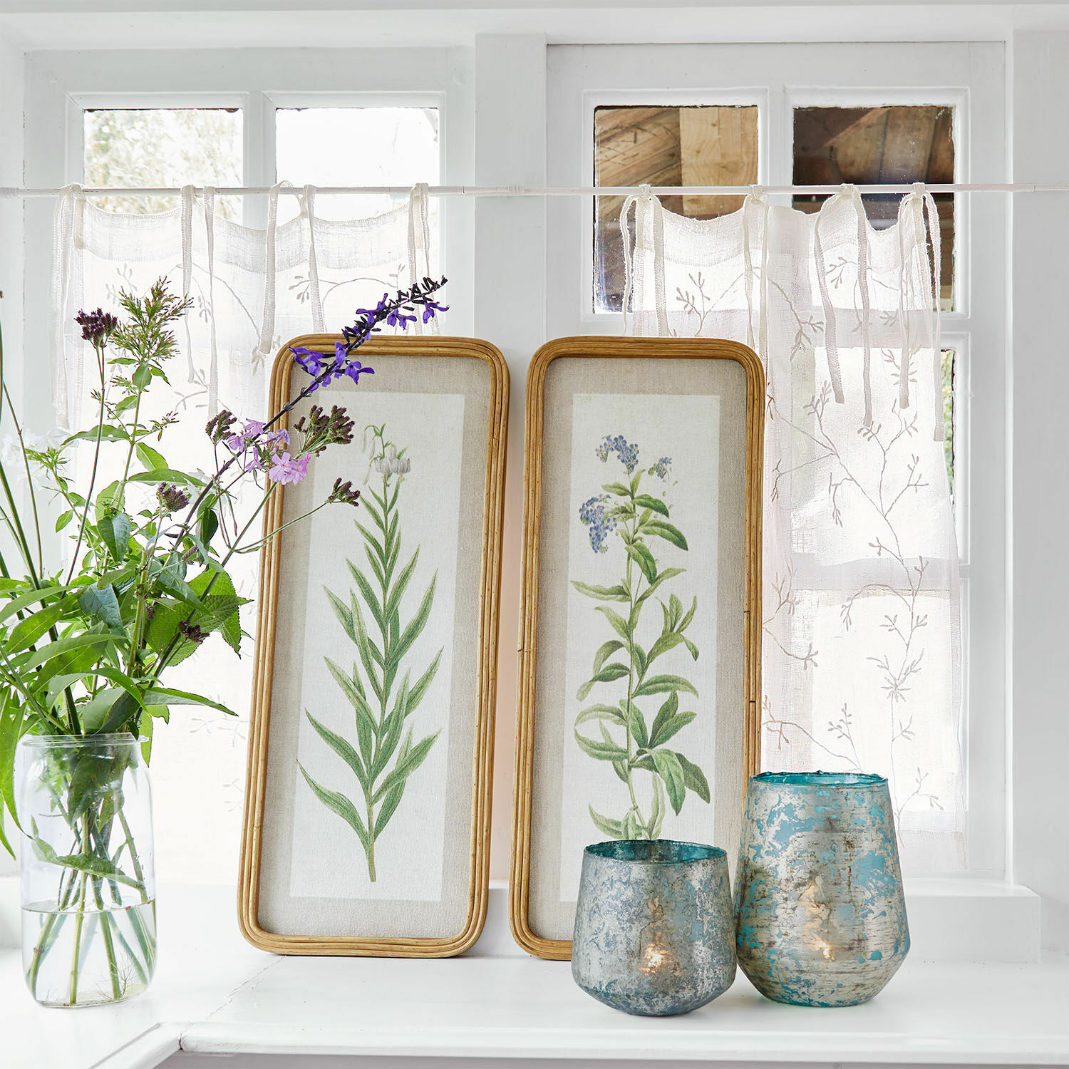 Afbeelding set van 2 Cenori Twee houten lijsten met botanische illustraties op een witte vensterbank met blauwe decoratieve windlichten