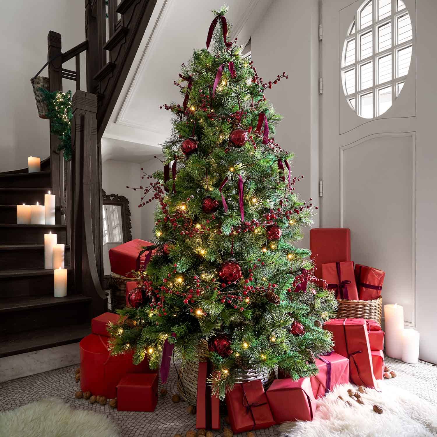Kerstboom met groene takken, rode versieringen en cadeaus in rood papier eromheen