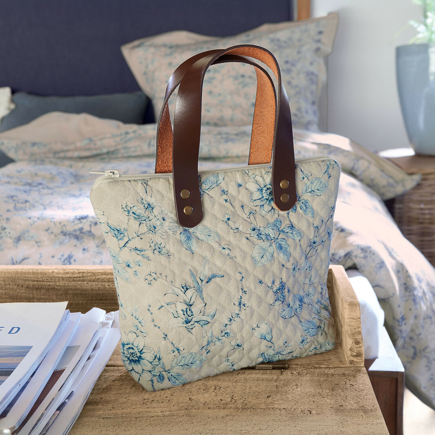 Beige gewatteerde tas met blauw bloemenpatroon en bruine leren handvatten op houten tafel