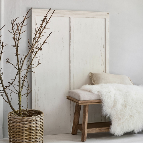 Rustieke houten bank met beige kussen en witte bontdeken naast een rieten mand met takken