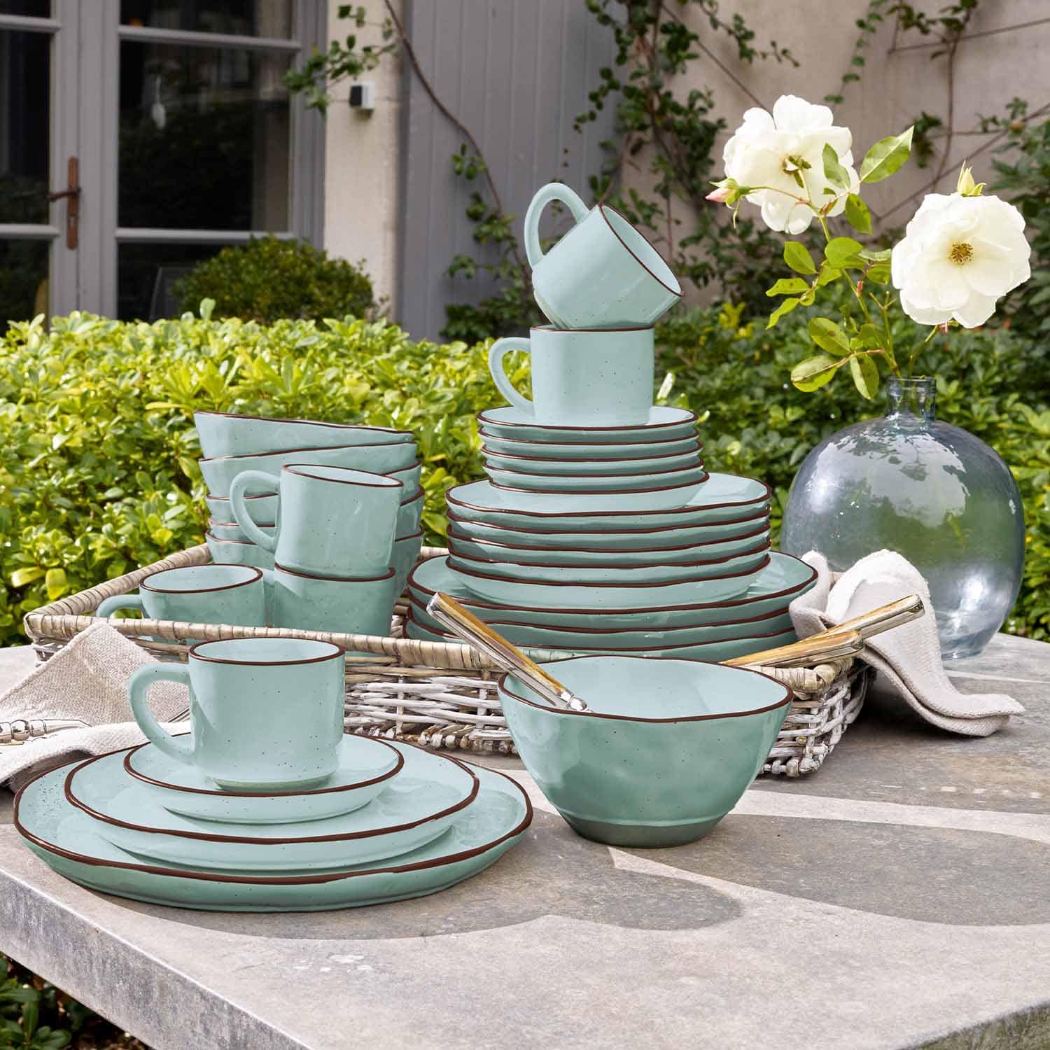 Mintgroen keramisch servies met bruine rand op een tuintafel geplaatst