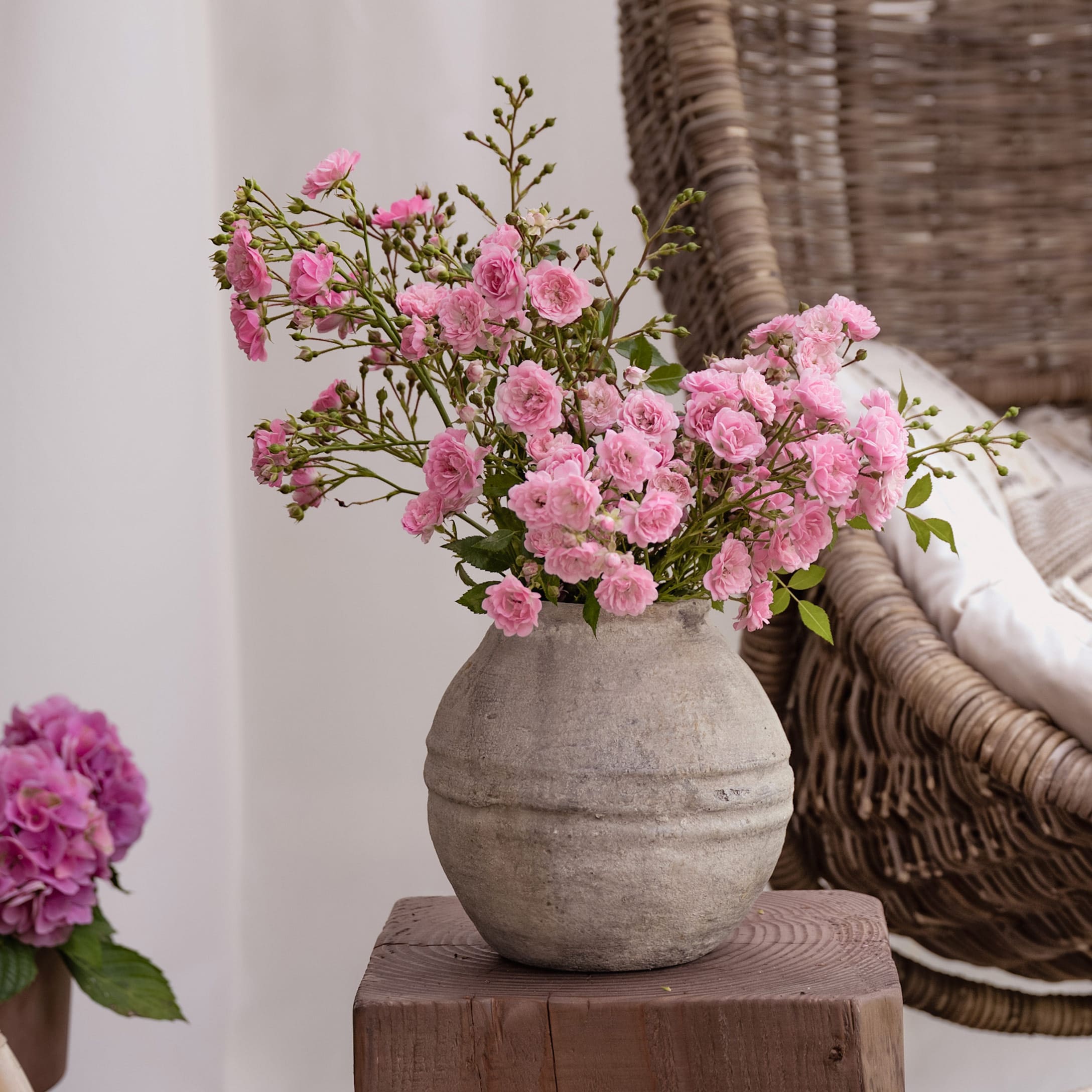 Grijze keramische vaas met roze bloemen op houten tafel in gezellige kamer