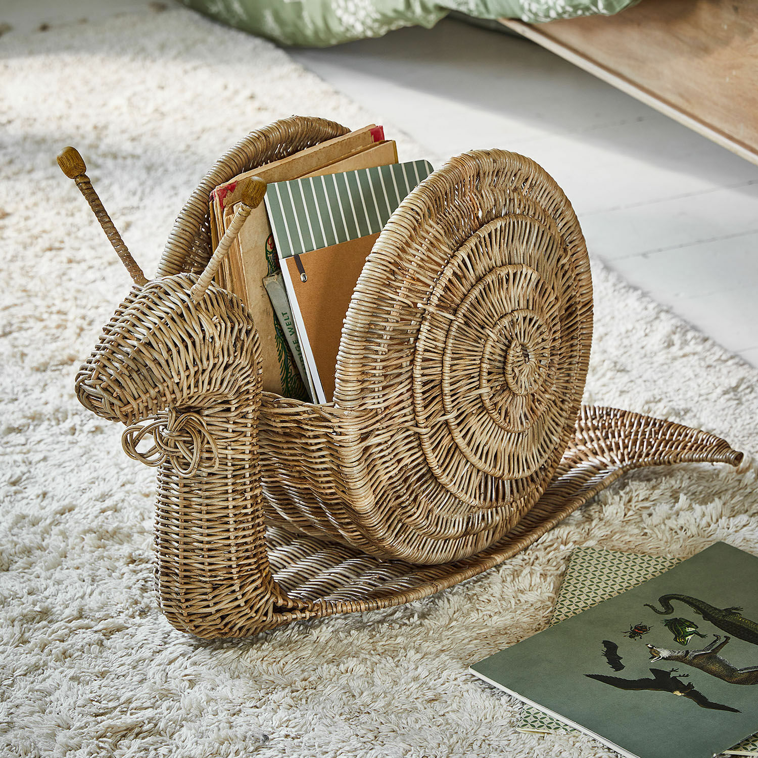 Mand Tigrelle Boekenhouder in de vorm van een slak van natuurlijk riet op een lichte vloerkleed voor interieur