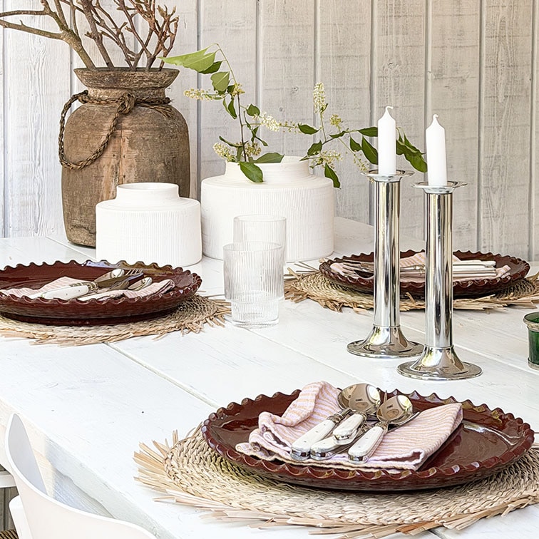 Witte houten tafel met bruine keramische borden en zilveren kandelaars op decoratieve placemats