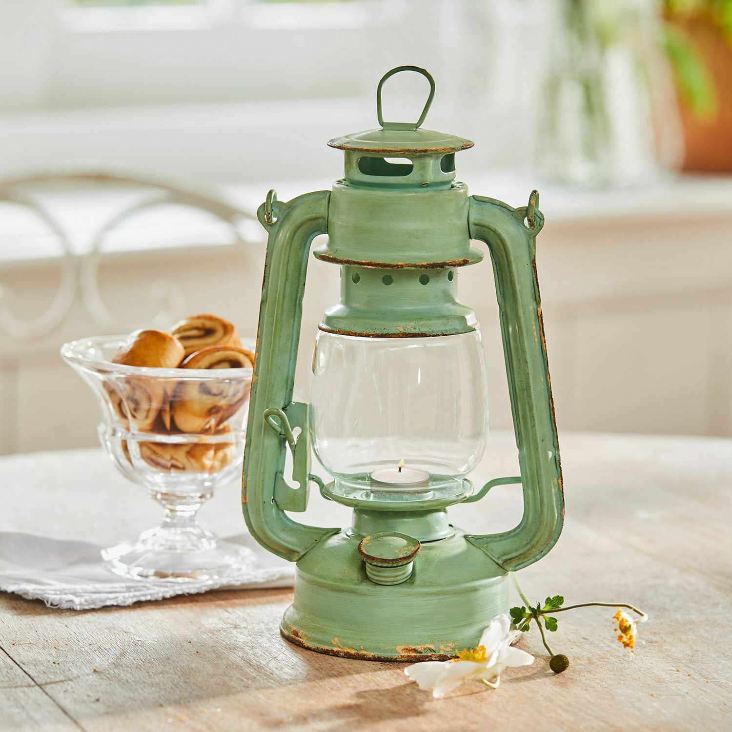 Lantaarn Clemence Groene metalen lantaarn met verouderd effect op houten tafel, gebak op de achtergrond