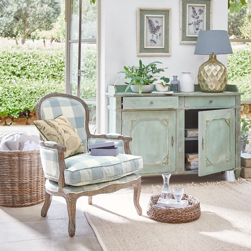 Stijlvolle geruite fauteuil met houten frame en groene kast met lamp in lichte woonkamer