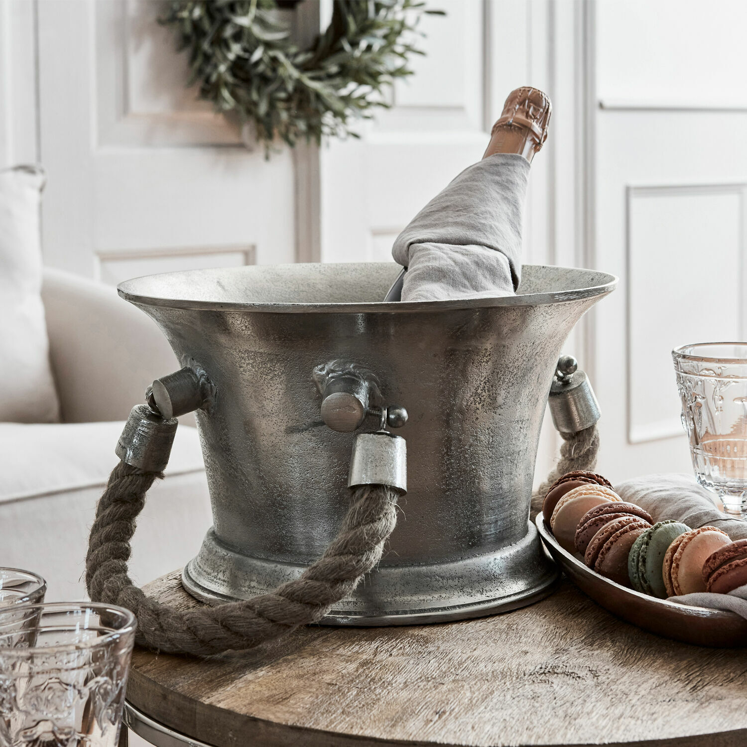 Metalen ijsemmer met dik touwhandvat en champagnefles in grijze hoes op houten tafel