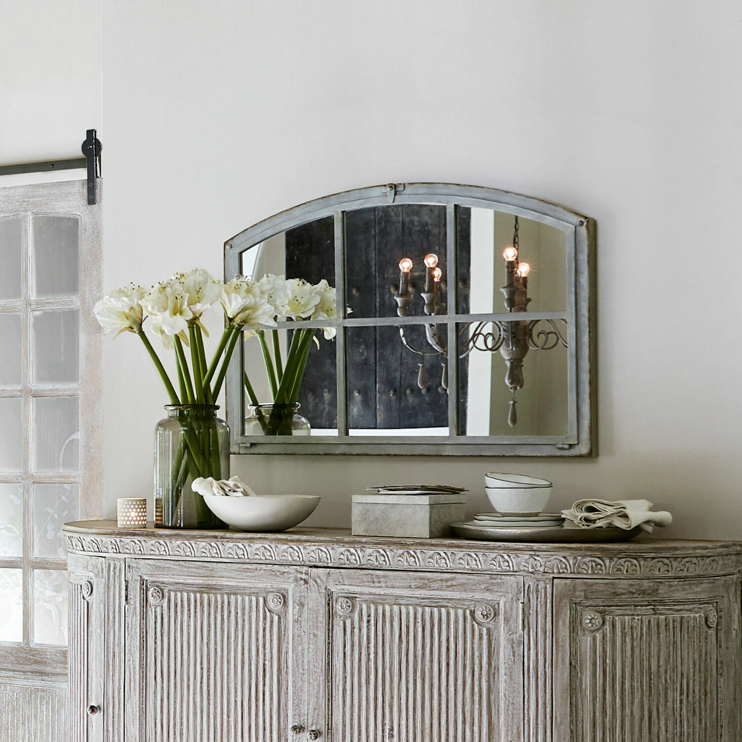 Rustieke witgewassen houten dressoir met spiegel en decoraties op het blad in lichte kamer