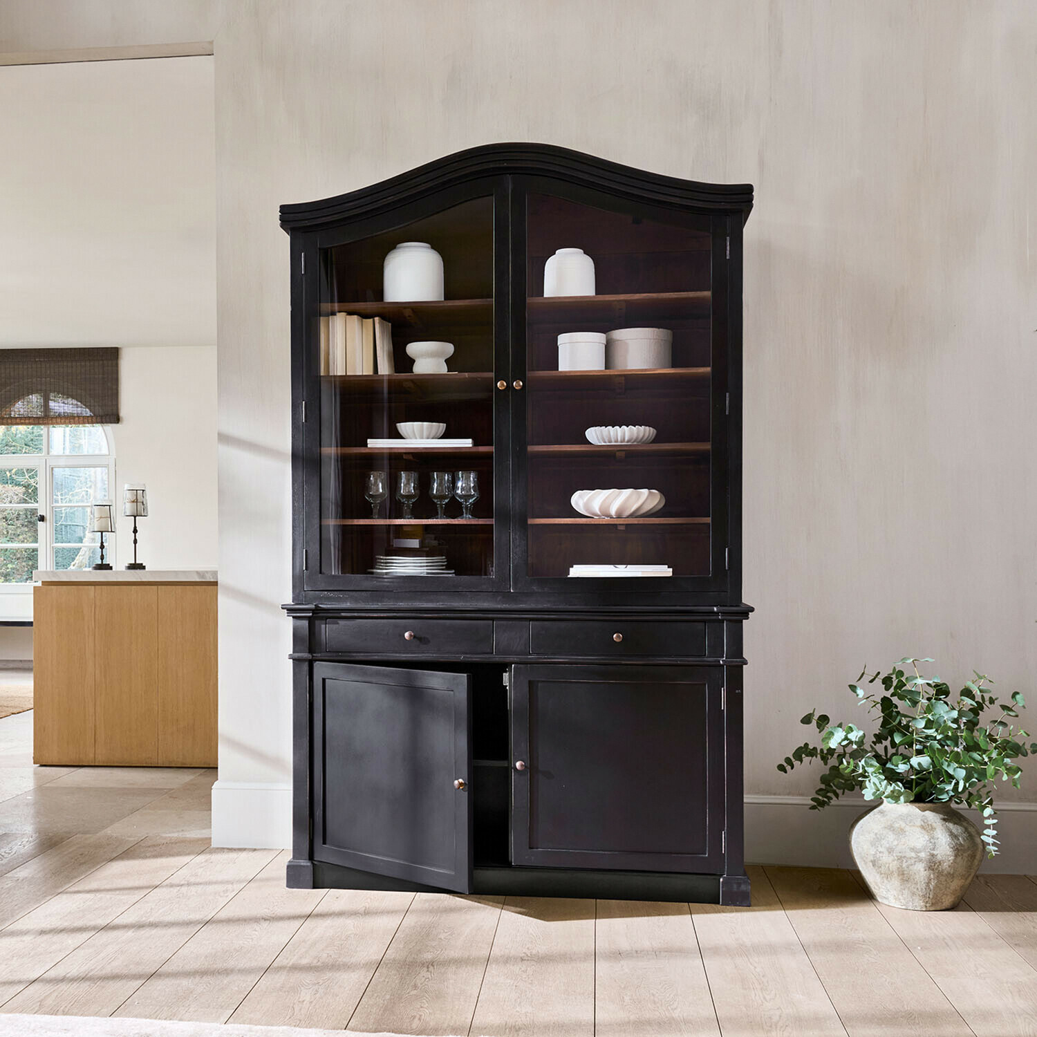 Zwarte houten vitrinekast met glazen deuren en witte keramiek en glazen op planken in woonkamer