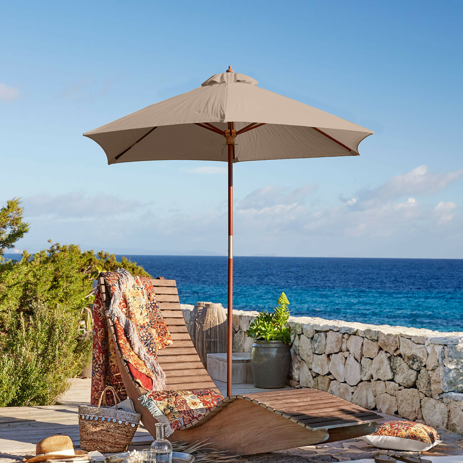 Parasol Enfield Houten ligstoel met beige parasol en kleurrijk plaid aan zee, terrasmeubilair