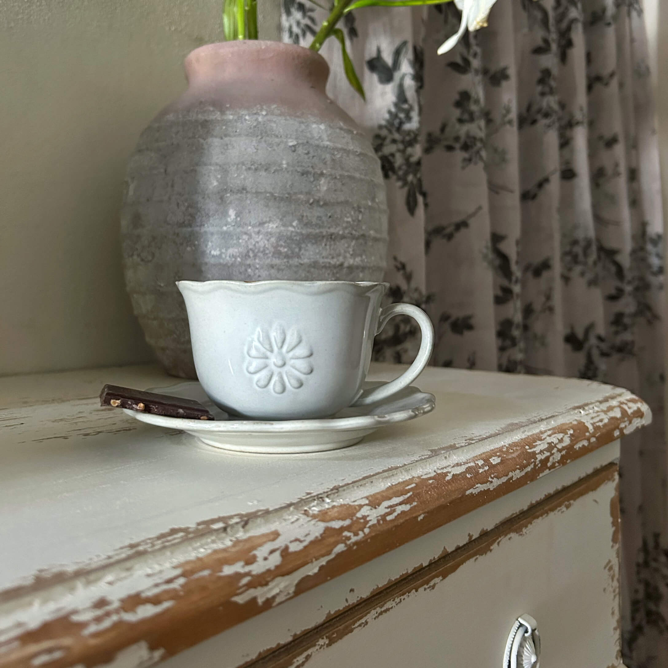 Witte keramische kop met schotel en stuk chocolade op verweerde houten tafel