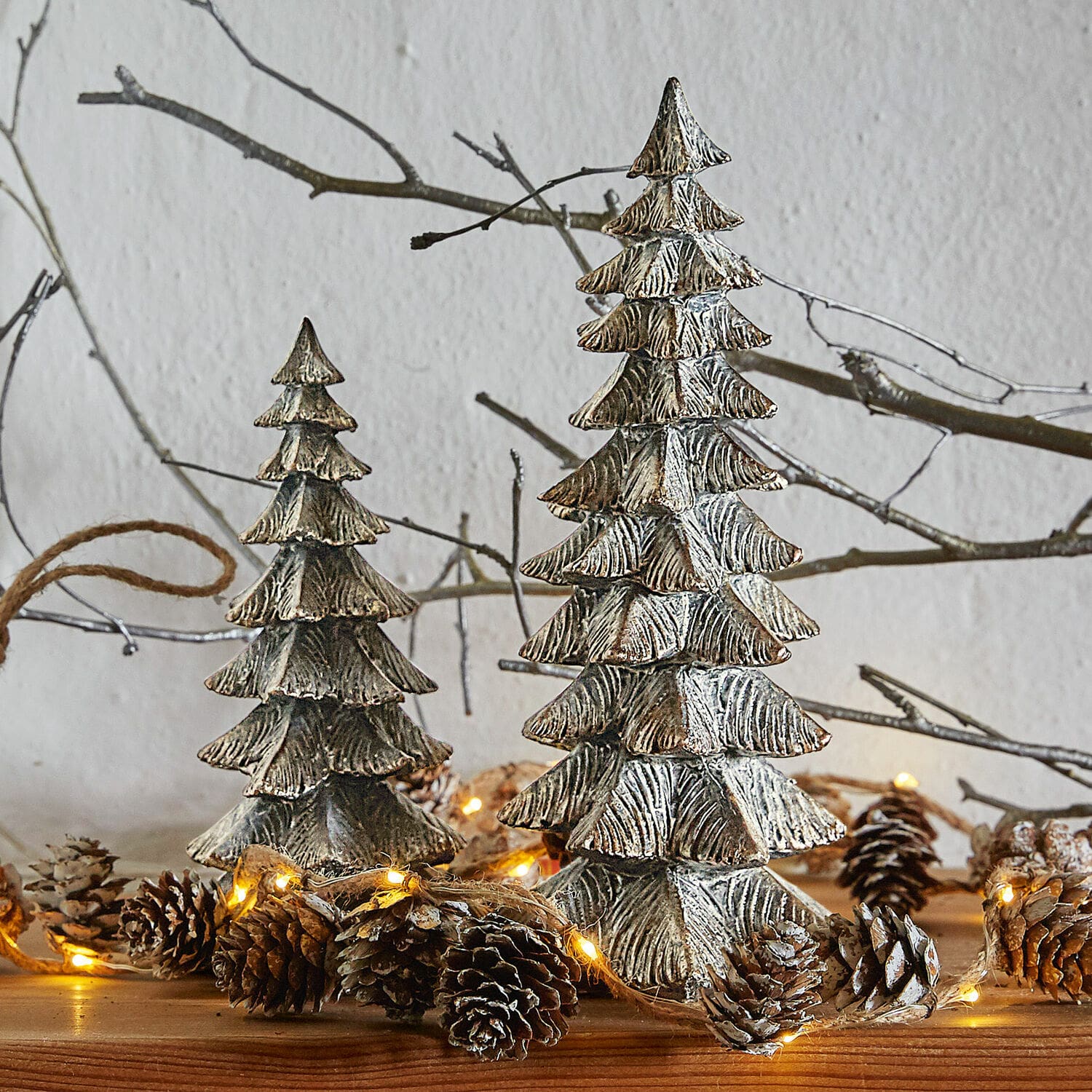 Sierboom set van 2 Calavi Decoratieve zilverkleurige metalen kerstbomen op houten tafel met lichtjes en dennenappels