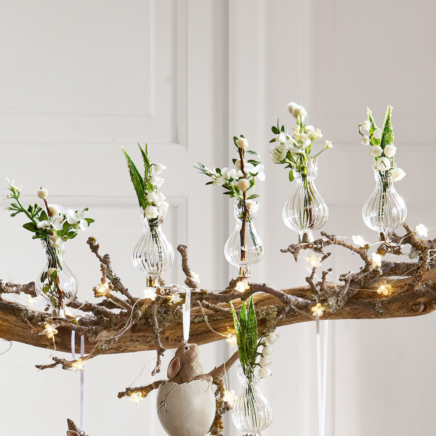 Transparante glazen vaasjes met witte bloemen op tak met LED-lichtjes als decoratie