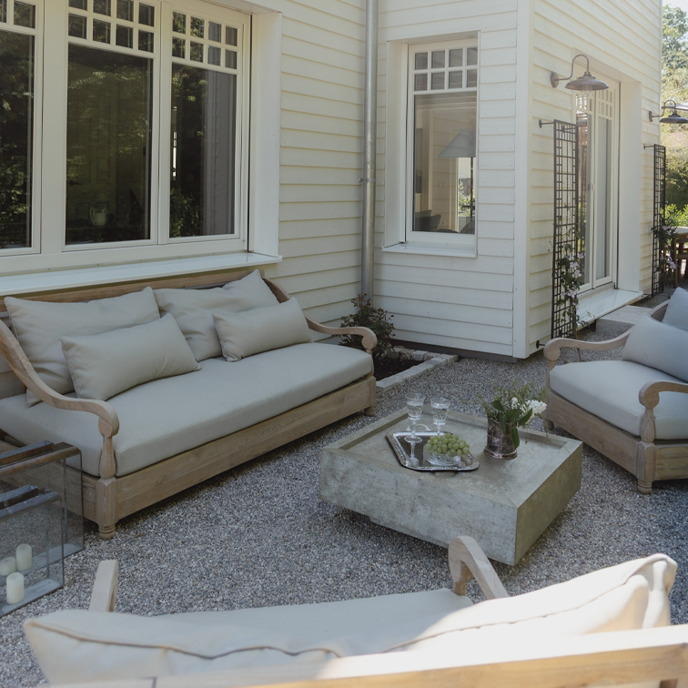 Tuinmeubelset van licht hout met grijze kussens op grindpatio voor wit huis