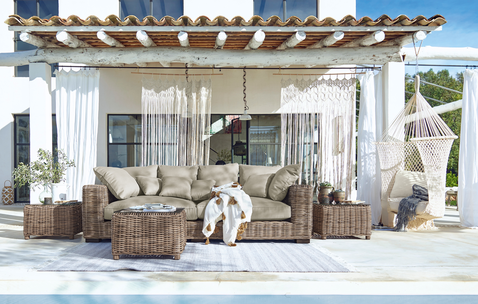 Tuinmeubelset van riet met beige kussens op terras met hangstoel en boho decoratie