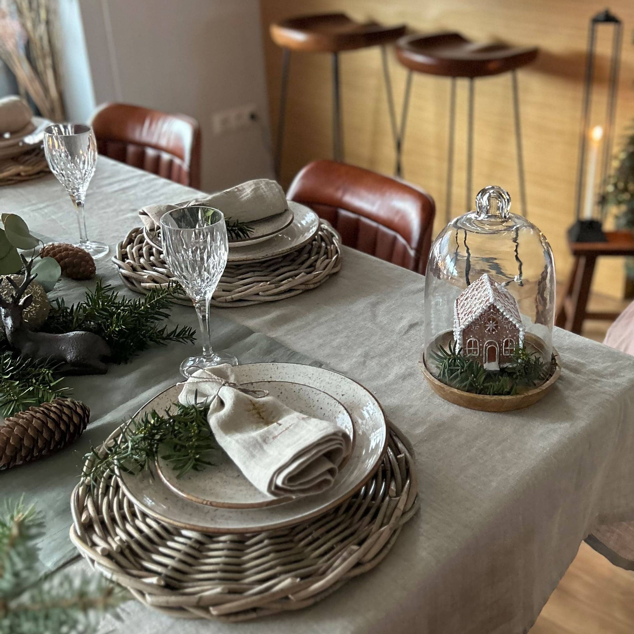 Stijlvol gedekte tafel met gevlochten placemats, keramische borden en kerstdecoratie met huisje onder glazen stolp