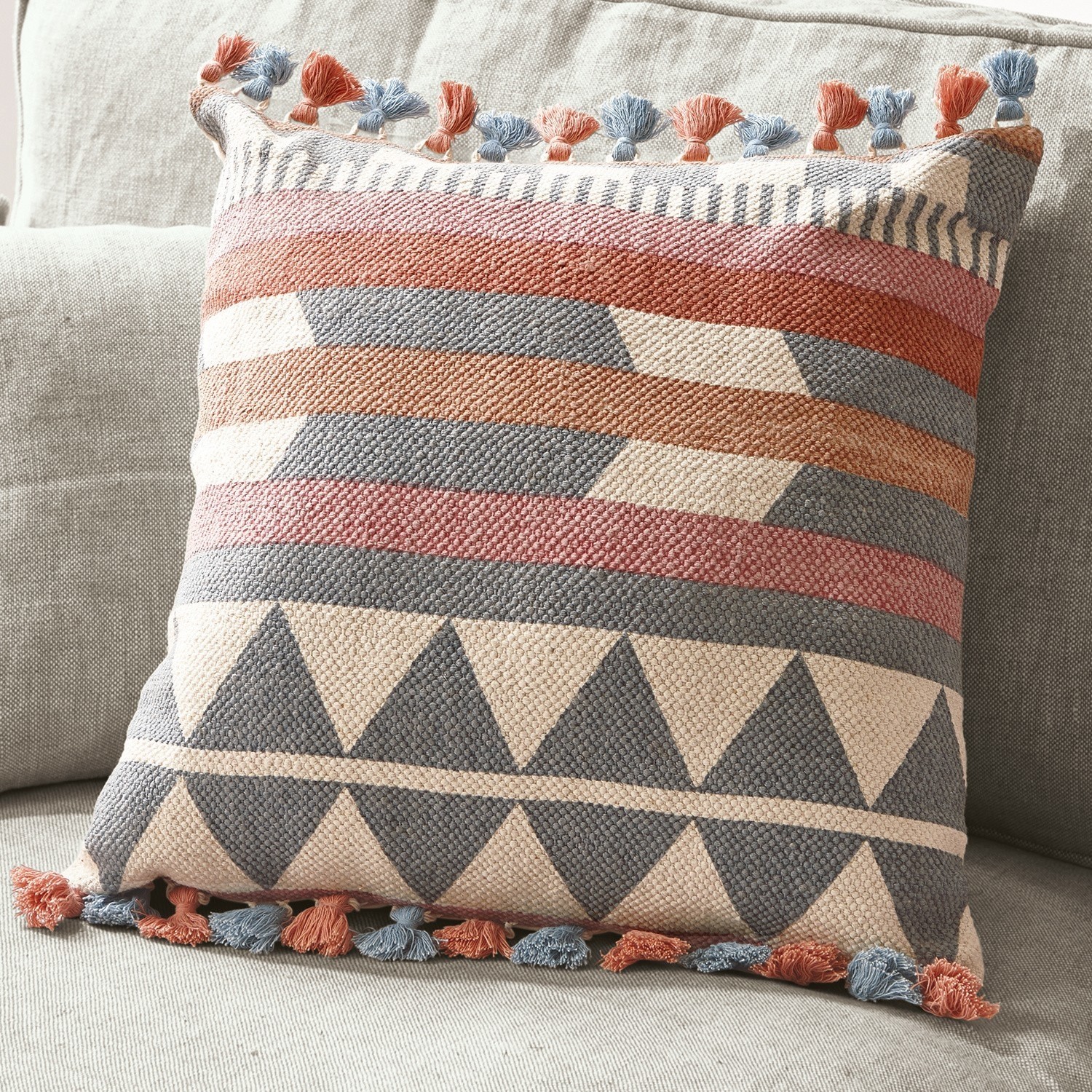 Decoratief katoenen kussen met geometrisch patroon en blauwe en oranje kwastjes op lichte bank