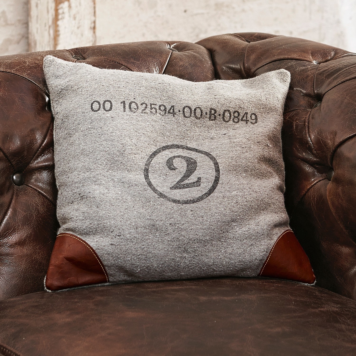 Grijs kussen met bruine leren hoeken op een bruine leren stoel, decoratief kussen voor woonkamer