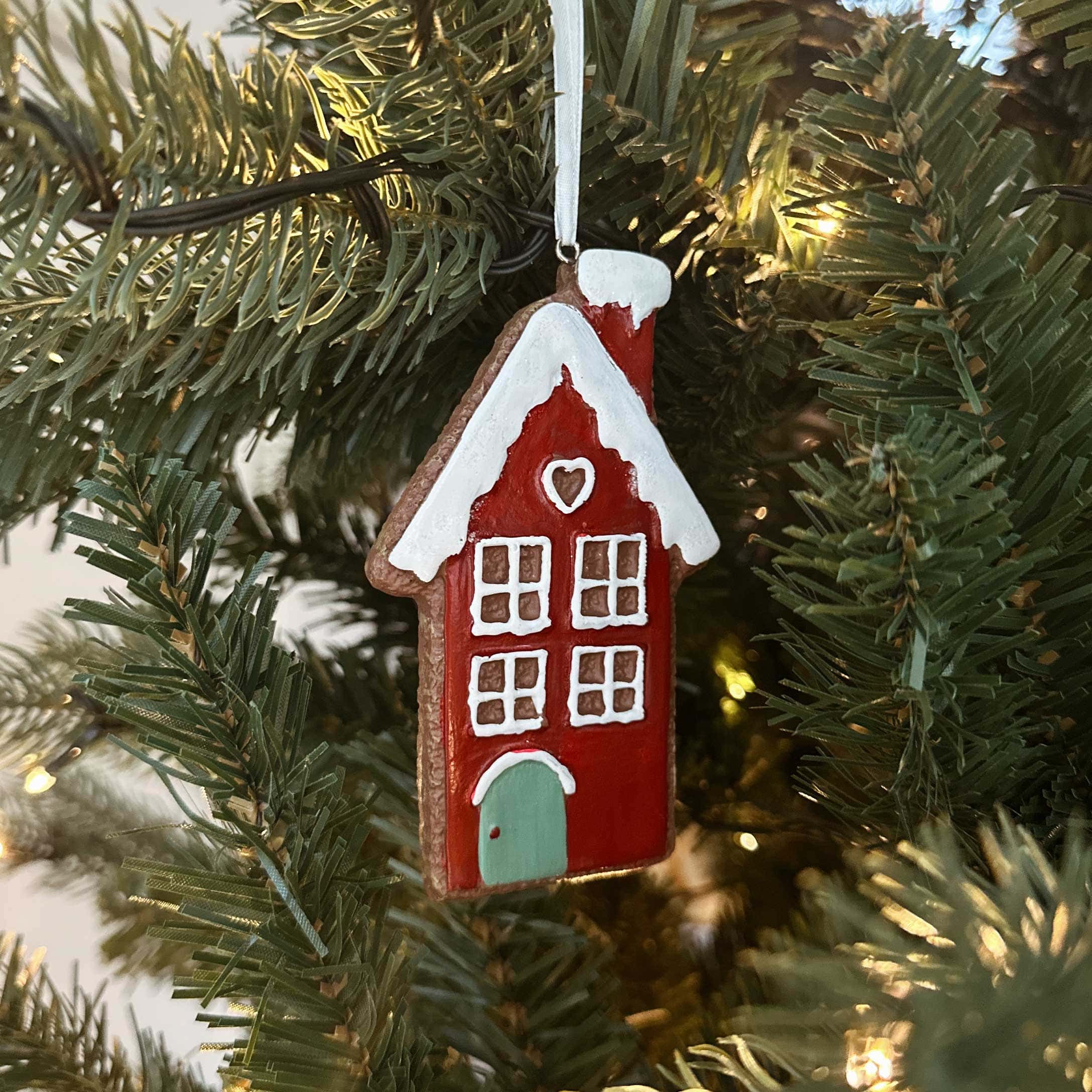 Rood keramisch kersthuisje met wit dak en groene deur hangend aan kerstboomtak