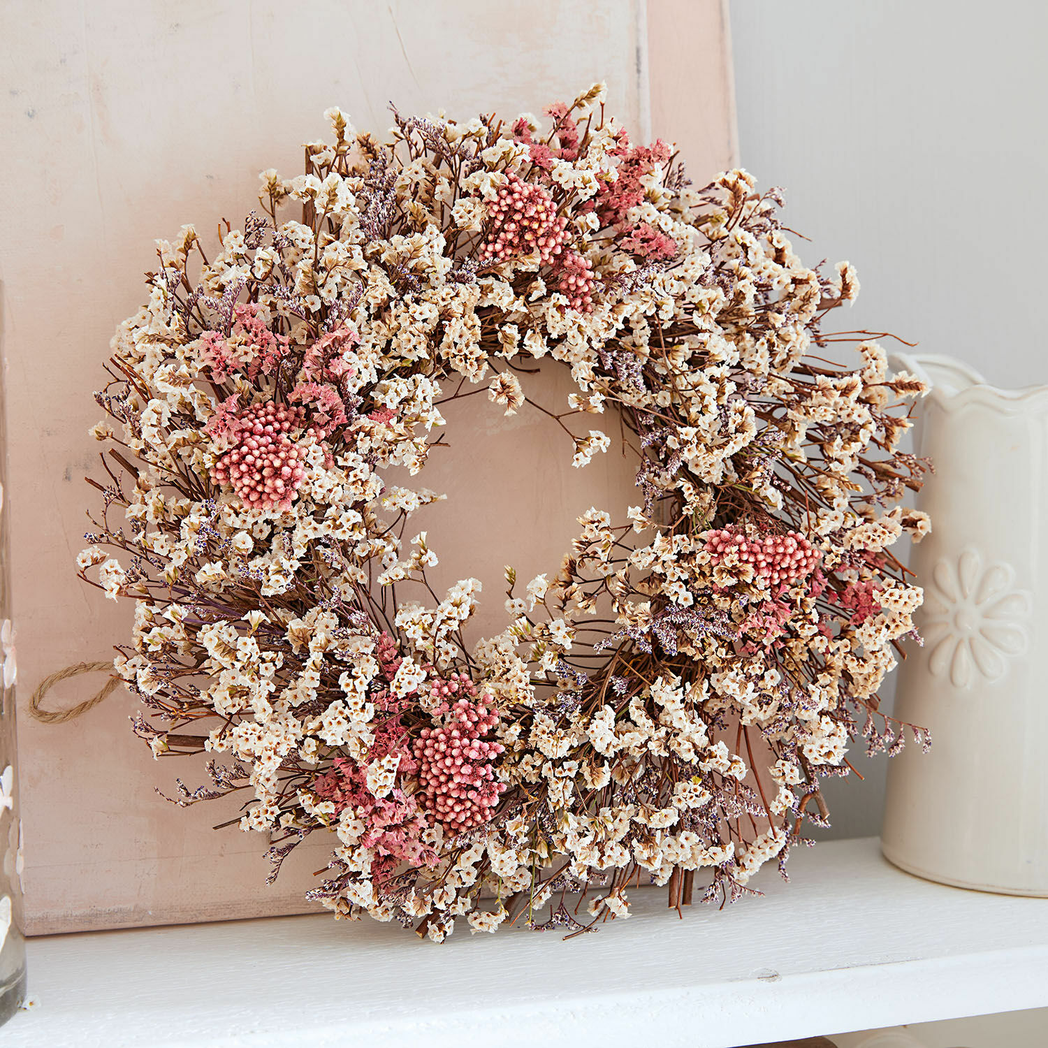 Decoratieve krans van gedroogde bloemen in crème- en rozetinten op lichte achtergrond