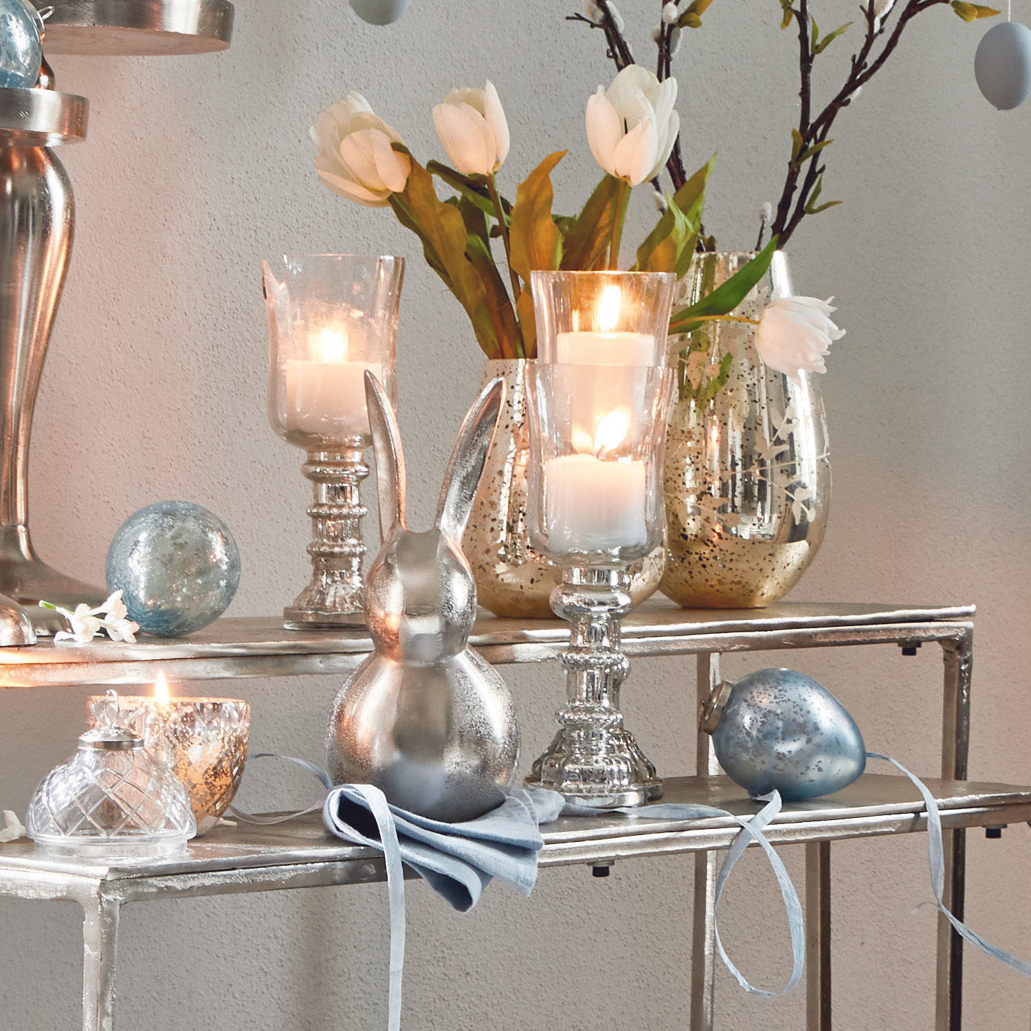 Decoratief zilveren konijn en glazen kandelaars met witte tulpen op metalen plank