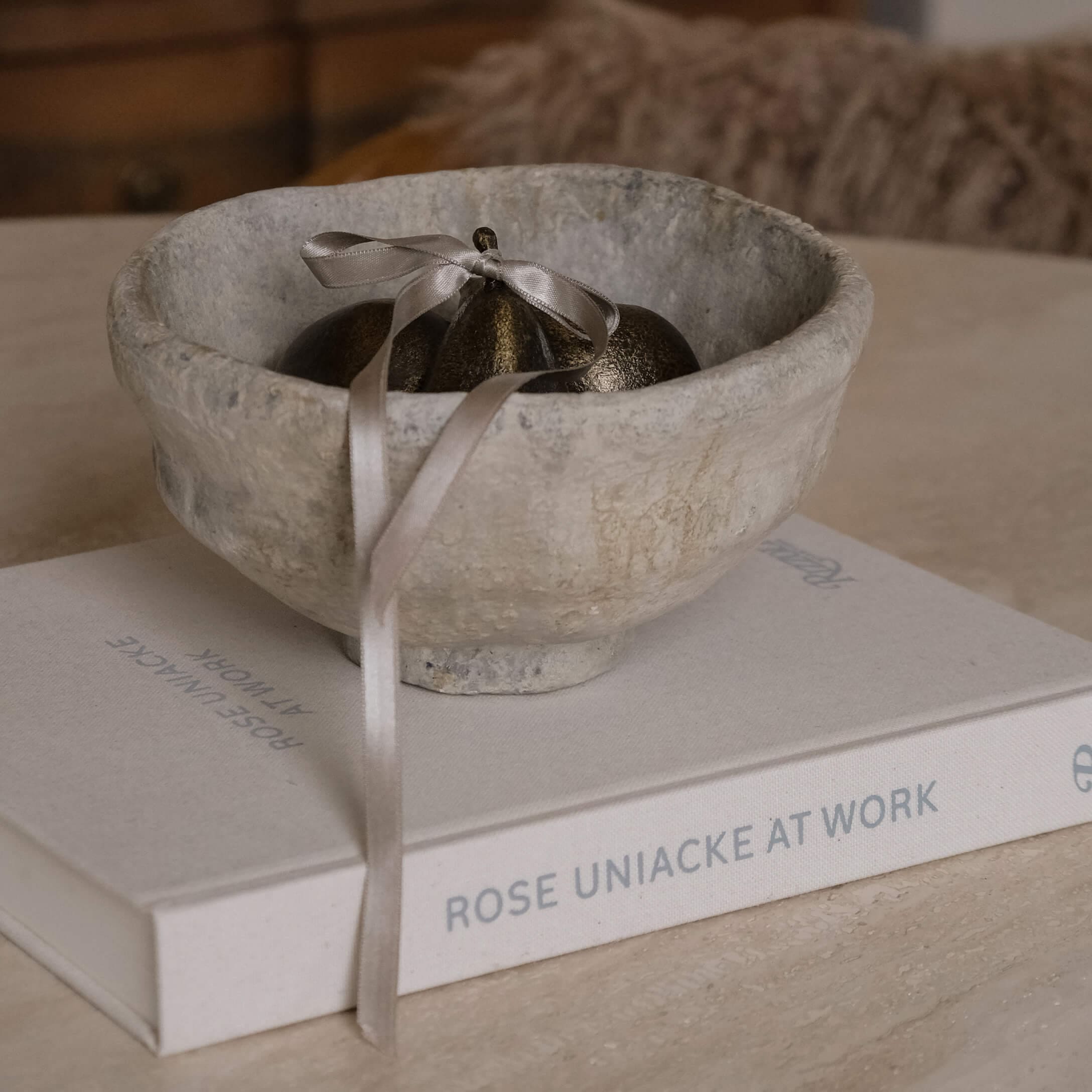 Decoratieve grijze stenen kom met metalen ornament en lint op een boek op tafel