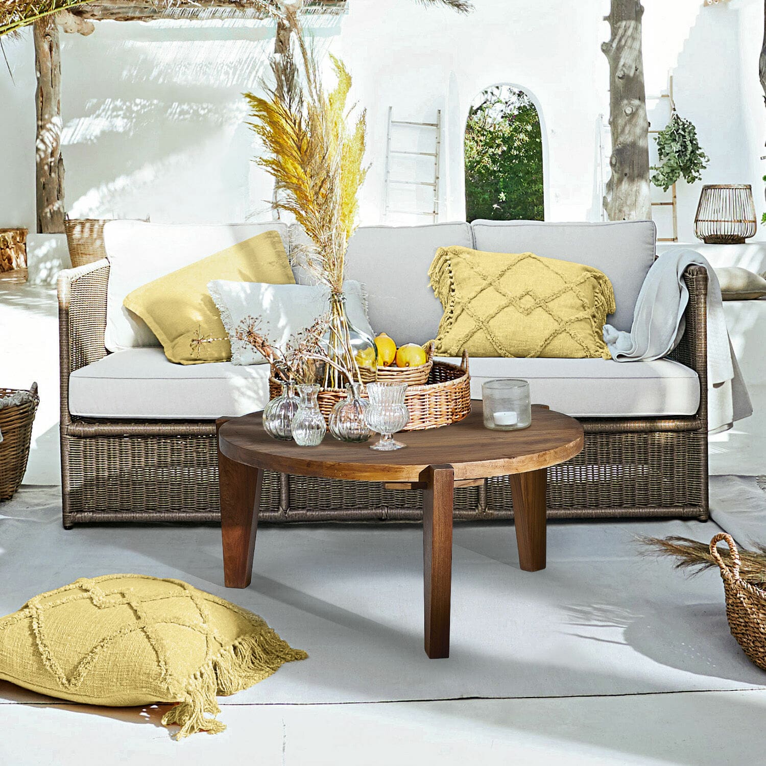 Bank Lesmont Woonruimte met rotan bank, lichtgrijze kussens en ronde houten salontafel op zonnig terras