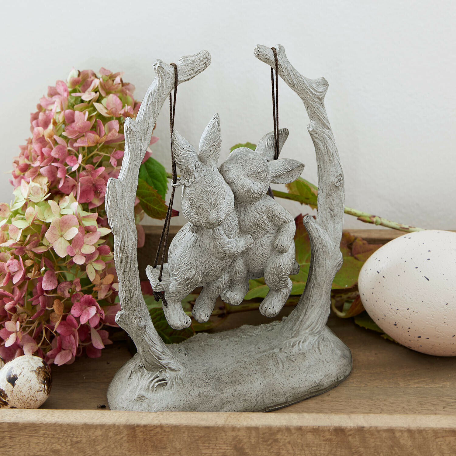 Grijs stenen beeld van twee konijnen op een schommel, paasdecoratie