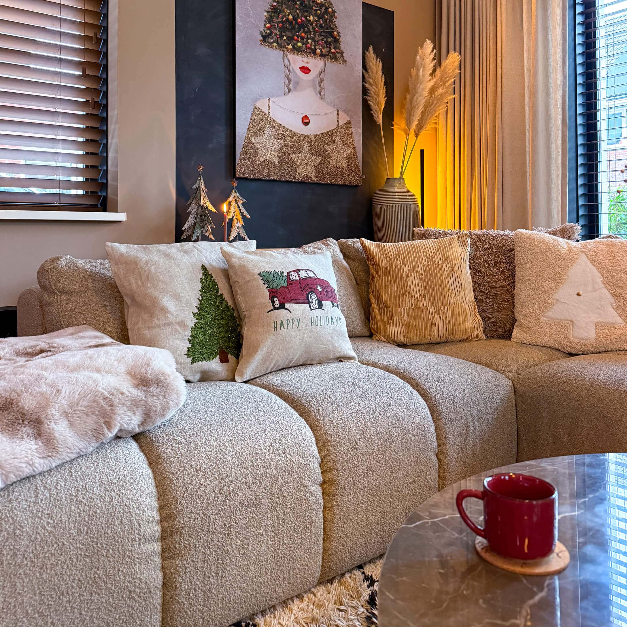 Beige bank met kerstkussens en rode mok op marmeren tafel in een gezellige woonkamer