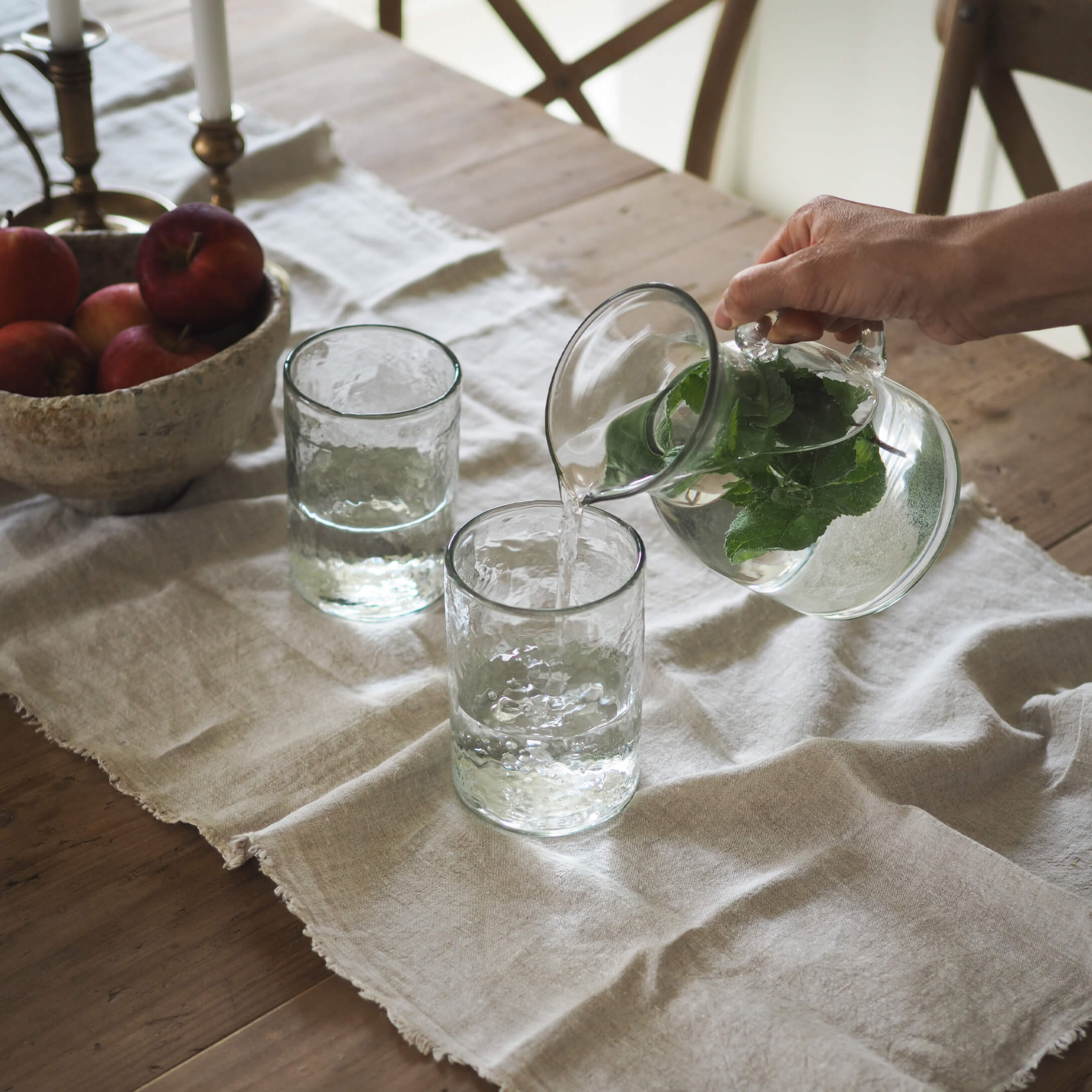 Glazen karaf met groene bladeren en twee glazen op een linnen tafelkleed op een houten tafel