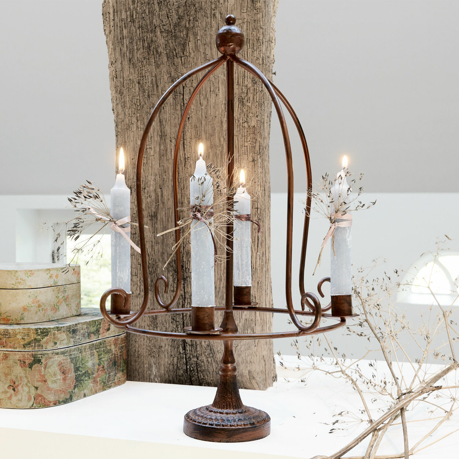 Metalen kandelaar in roestkleur met vier witte kaarsen en gedroogde planten als decoratie