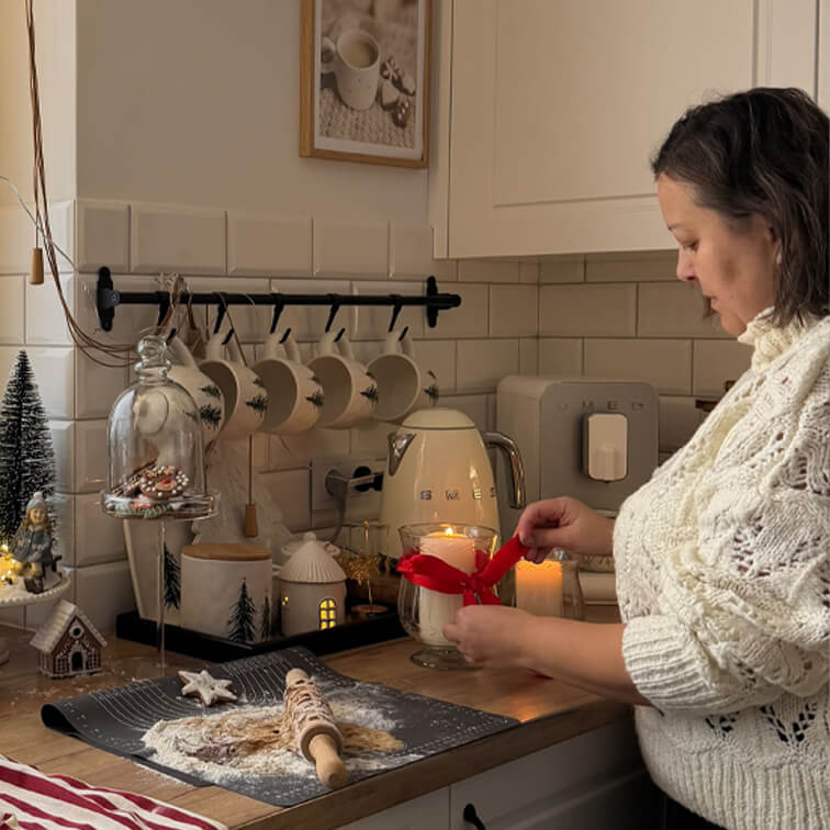 Vrouw in witte trui versiert kaars met rood lint in gezellige keuken met bakgerei