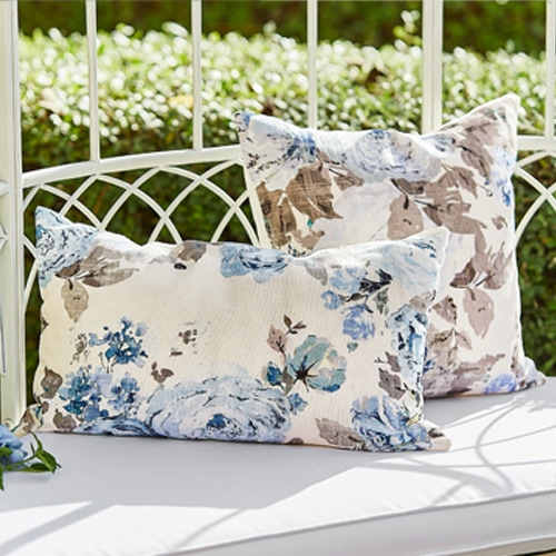 Decoratieve kussens met blauw-beige bloemenpatroon op een witte metalen tuinbank